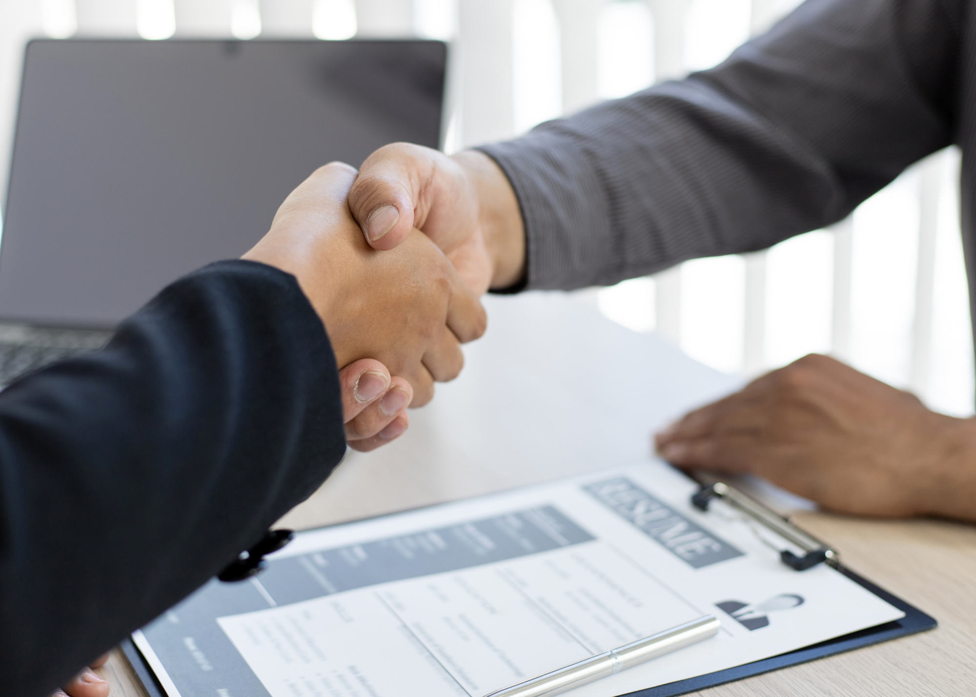 Two people sitting at desk shaking hands.