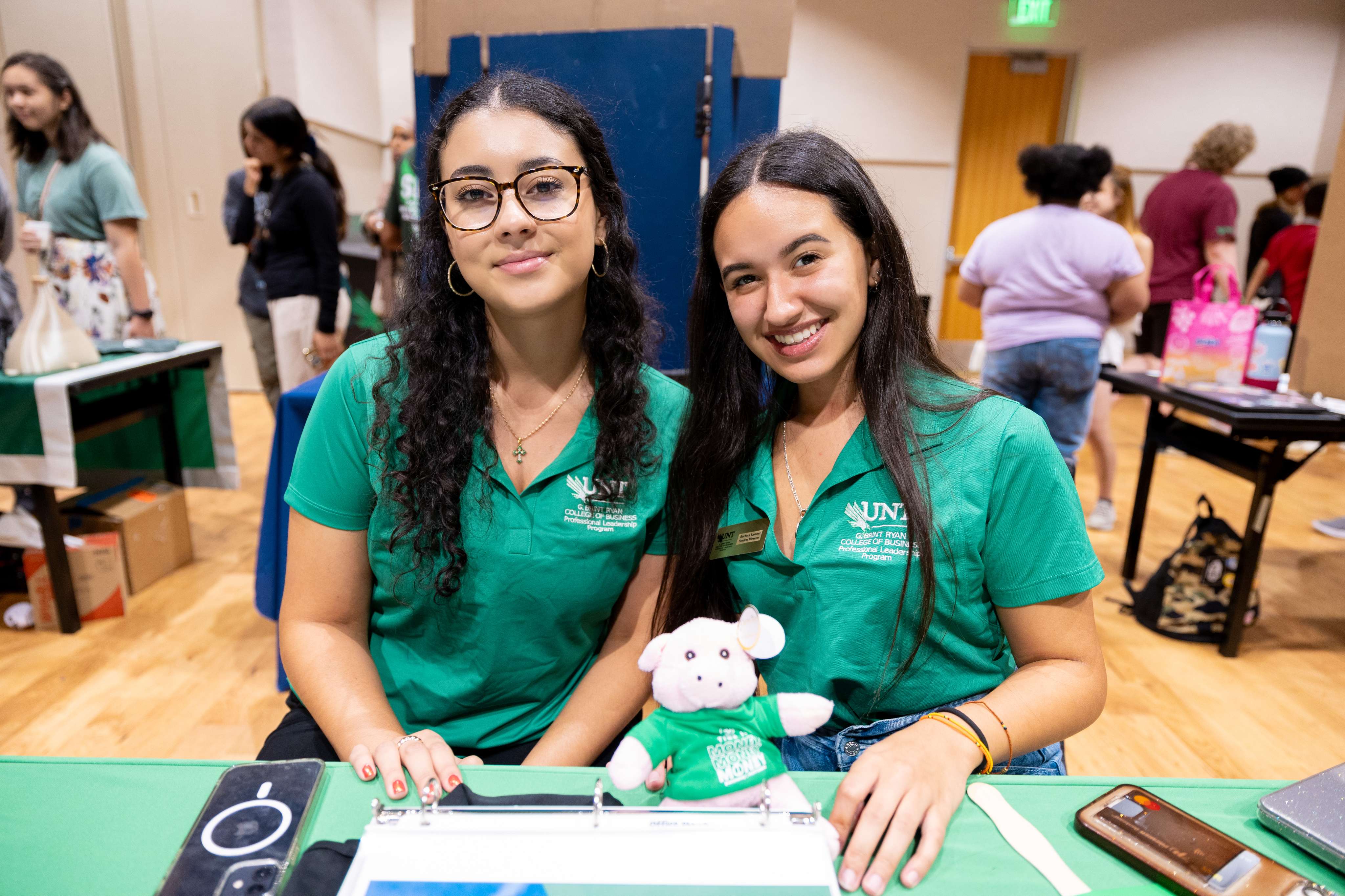 Two girls at mean green blowout with paperwork and UNT toy