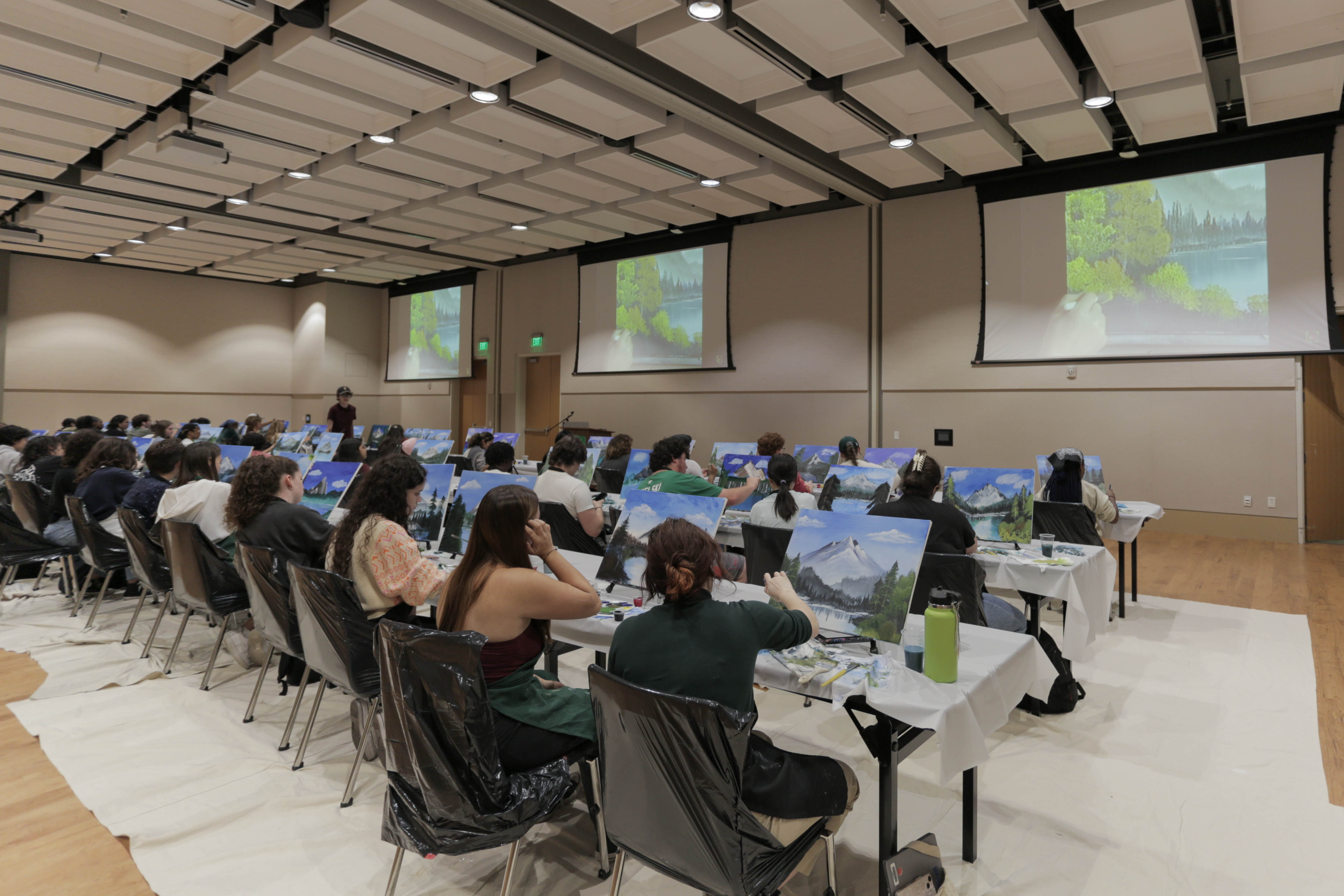 image of students painting a mountainous landscape scene while following along to a bob ross video